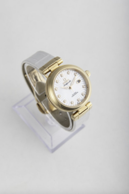 A gold and white Omega watch on a clear display against a white background